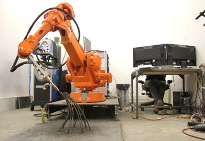 Một robot đang đúc, “in” nhiều thanh kim loại mảnh. Bên cạnh đó là các máy hút mùi, tiêu âm, thoát khói cùng vòi thổi nguội kim loại sau khi đúc.