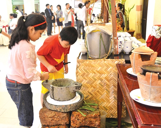 Các em bé thích thú với cối xay bột gạo thủ công để đúc bánh xèo tại Nhà hàng Sông Trà.