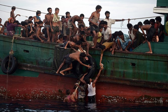 Người di cư đang chuyền tay nhau thức ăn do trực thăng Thái thả xuống biển - Ảnh: AFP