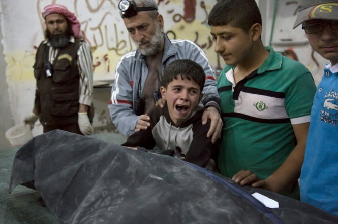 Một bé trai người Syria bên cạnh thi thể người thân của em thiệt mạng trong vụ không kích tại Aleppo ngày 27-4. Ảnh: AFP