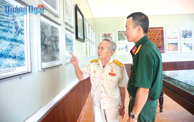 Nguyên Phó Bí thư Huyện ủy Trà Bồng Hồ Văn Lâm (trái) từng tham gia Khởi nghĩa Trà Bồng giới thiệu về cuộc khởi nghĩa thông qua những bức ảnh, hiện vật lịch sử.
