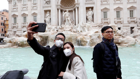 Du khách đeo khẩu trang chụp hình tại một điểm du lịch ở Ý - Ảnh: SKY