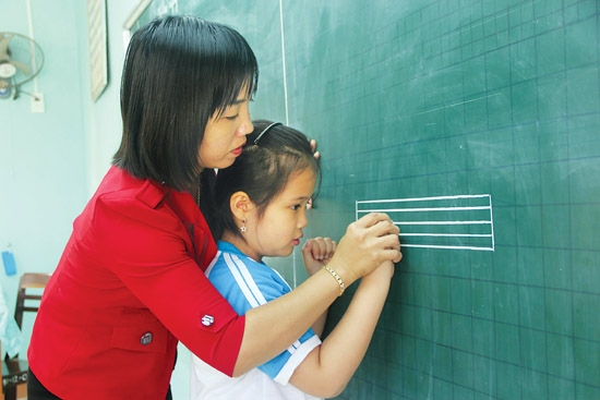 Cô giáo Trường Tiểu học Nguyễn Nghiêm (TP.Quảng Ngãi) giúp học sinh uốn nắn từng con chữ.  