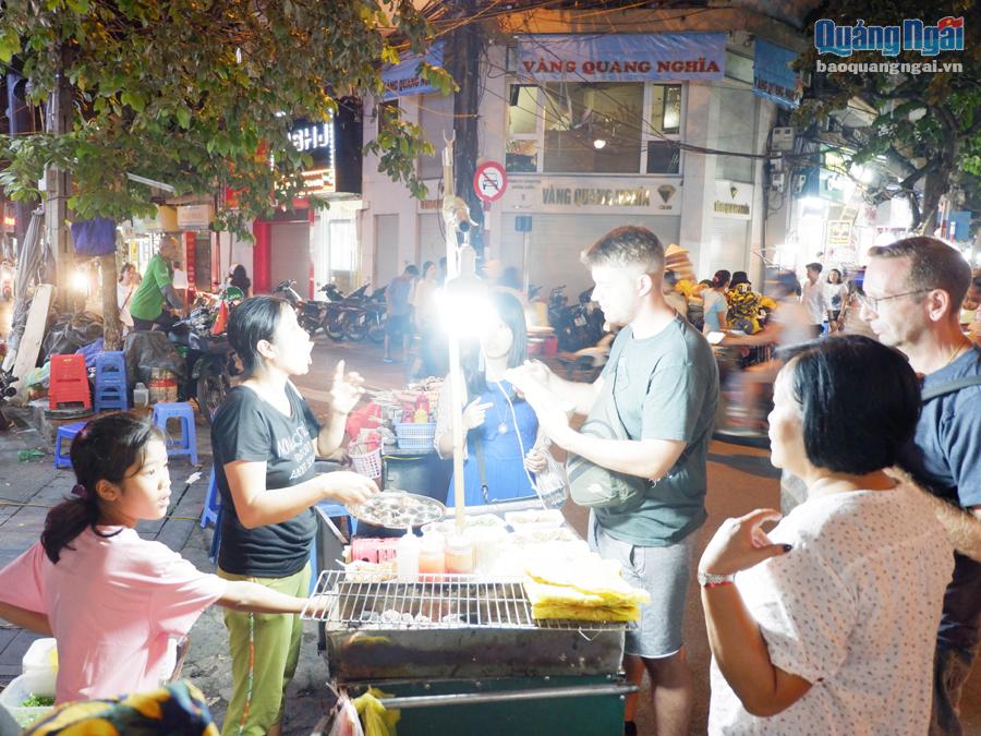 Du khách nước ngoài khám phá ẩm thực Hà Nội ở phố đi bộ.