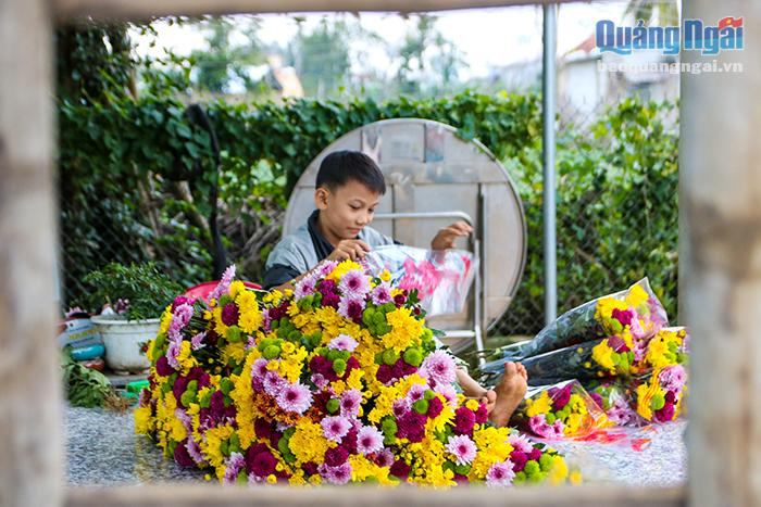 Một em nhỏ phụ mẹ gói hoa vào giấy kiếng trước lúc giao cho thương lái