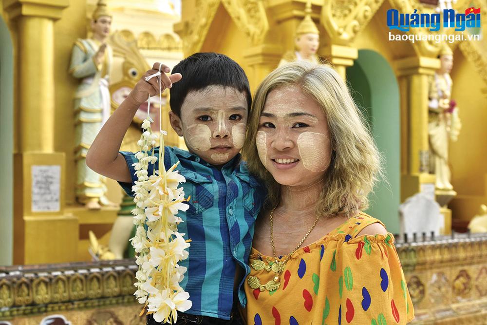 Hai mẹ con đi lễ chùa với chùm hoa ngọc lan và gương mặt được trang điểm bằng bột Thanakha.
